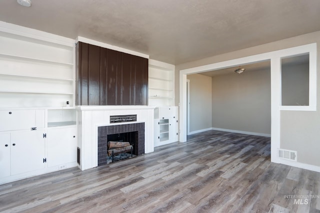 unfurnished living room with baseboards, a fireplace, visible vents, and wood finished floors