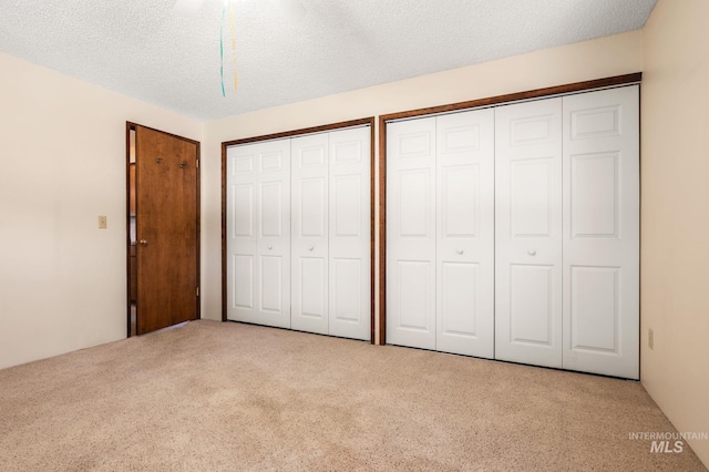 unfurnished bedroom featuring a textured ceiling, light colored carpet, ceiling fan, and multiple closets