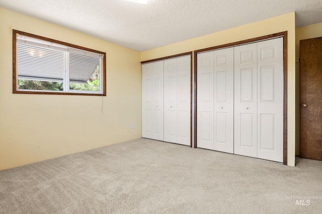 unfurnished bedroom with a textured ceiling, two closets, and light colored carpet