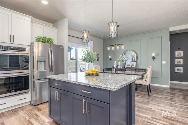 kitchen with appliances with stainless steel finishes, white cabinets, light wood-type flooring, light stone countertops, and a center island