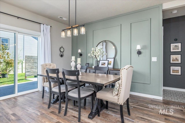 dining room with wood finished floors, healthy amount of natural light, baseboards, and a decorative wall