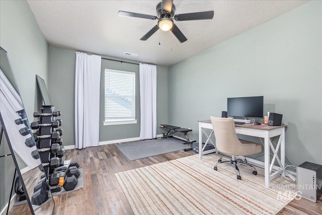 home office with wood finished floors, ceiling fan, a textured ceiling, and baseboards