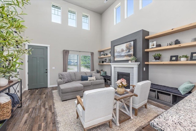 living area with a towering ceiling, dark wood-style flooring, a brick fireplace, and baseboards