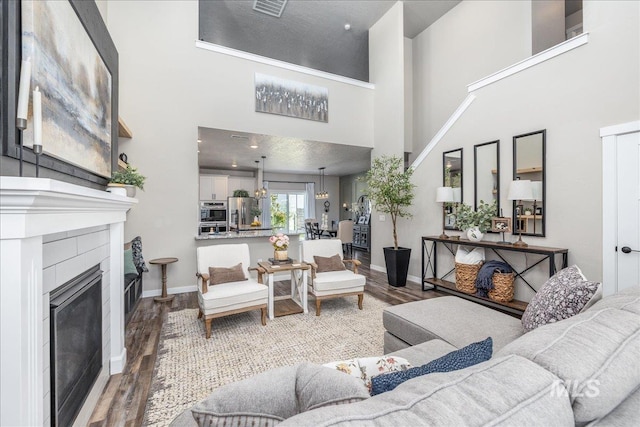living room with wood finished floors, a towering ceiling, a fireplace, and baseboards