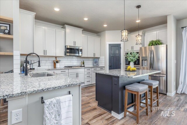 kitchen featuring appliances with stainless steel finishes, a kitchen bar, a sink, tasteful backsplash, and white cabinets