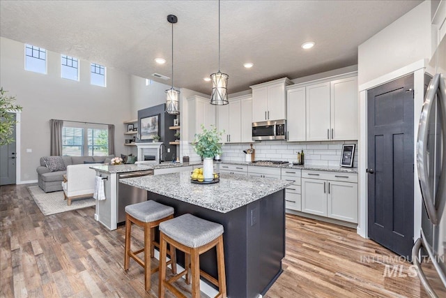 kitchen featuring stainless steel appliances, a center island, light wood finished floors, backsplash, and white cabinetry