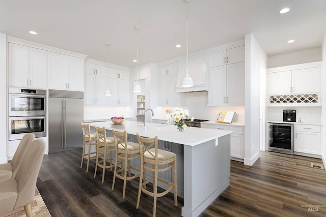 kitchen with an island with sink, a sink, stainless steel appliances, dark wood-type flooring, and wine cooler