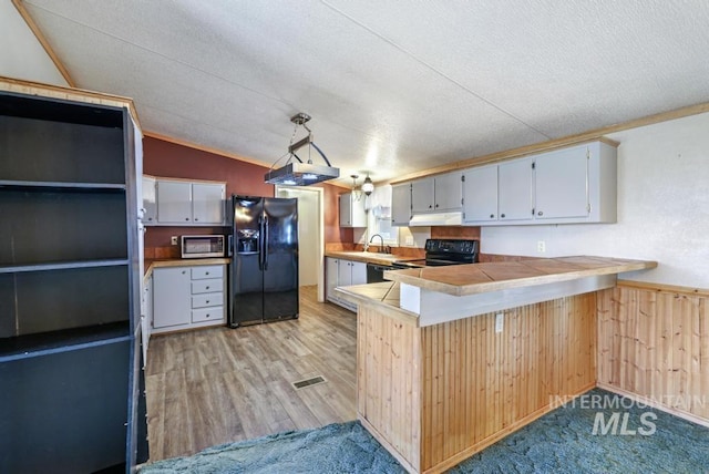 kitchen featuring vaulted ceiling, a sink, black appliances, a peninsula, and under cabinet range hood