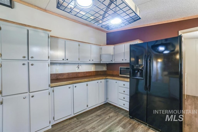 kitchen featuring black fridge with ice dispenser, stainless steel microwave, dark wood-style floors, and dark countertops