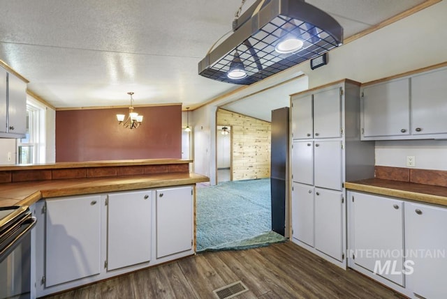 kitchen with a chandelier, wood walls, range with electric cooktop, dark wood-type flooring, and visible vents