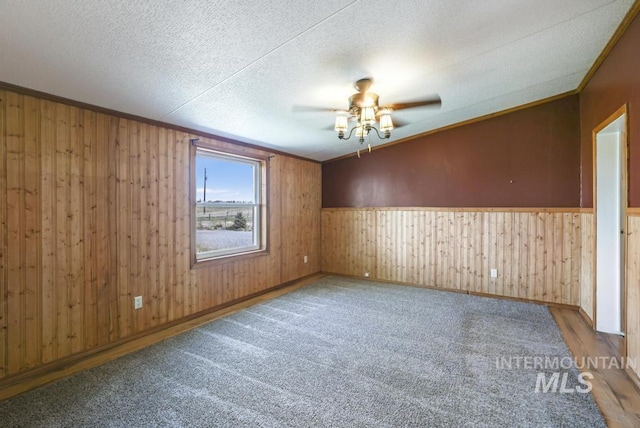 unfurnished room with ceiling fan, a textured ceiling, crown molding, a wainscoted wall, and wooden walls