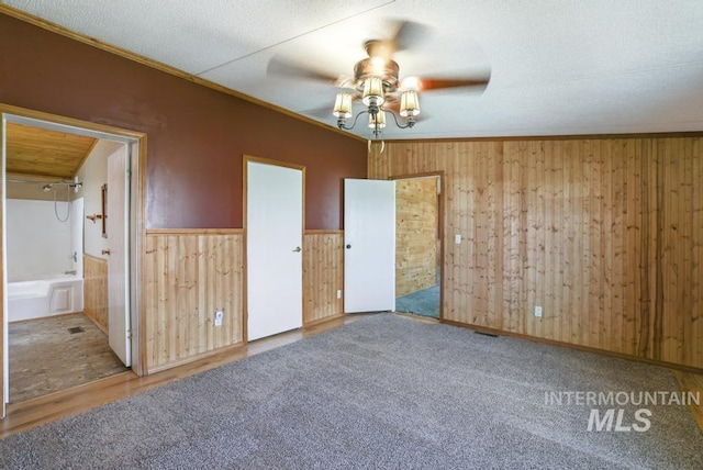 unfurnished room featuring wooden walls, a ceiling fan, crown molding, and wainscoting