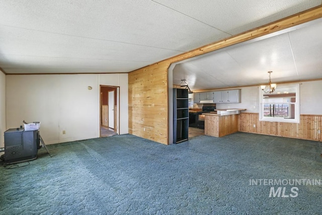 unfurnished living room featuring an inviting chandelier, carpet flooring, and wooden walls