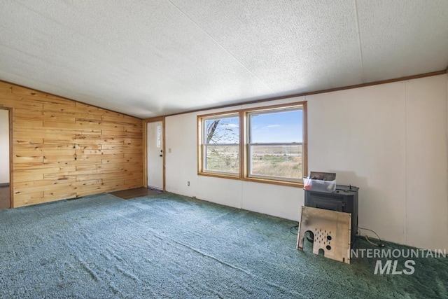 carpeted empty room with wood walls, a textured ceiling, and lofted ceiling
