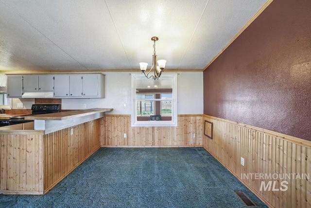 kitchen with an inviting chandelier, electric range, wainscoting, wooden walls, and under cabinet range hood