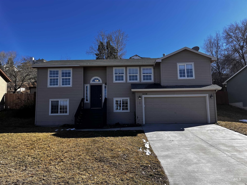 split foyer home featuring driveway, a garage, and fence