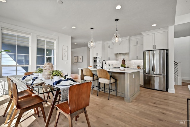 kitchen featuring a center island with sink, light wood finished floors, light countertops, appliances with stainless steel finishes, and backsplash