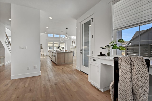 kitchen with an island with sink, recessed lighting, white cabinetry, decorative light fixtures, and light wood-type flooring