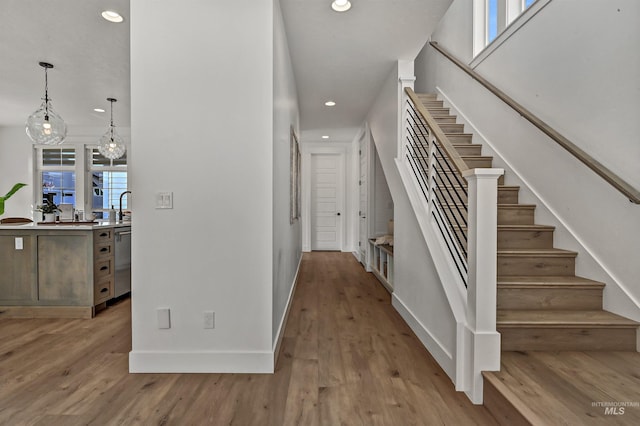 hallway with a sink, recessed lighting, stairway, light wood-style floors, and baseboards