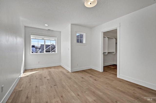 unfurnished bedroom with a closet, baseboards, light wood-style flooring, and a spacious closet