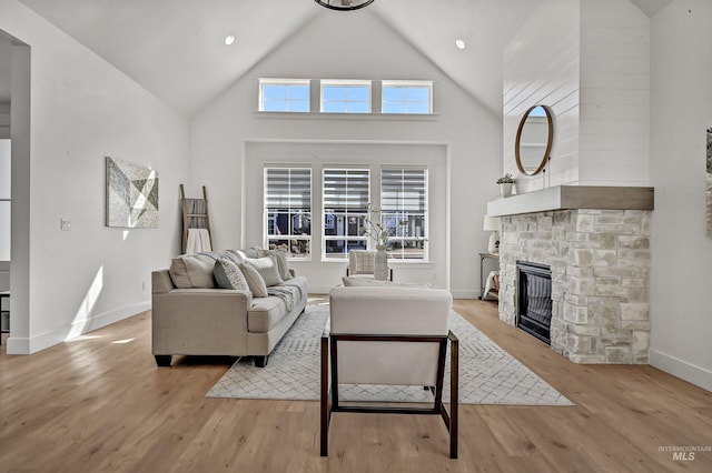 living area with a stone fireplace, light wood-style floors, baseboards, and high vaulted ceiling