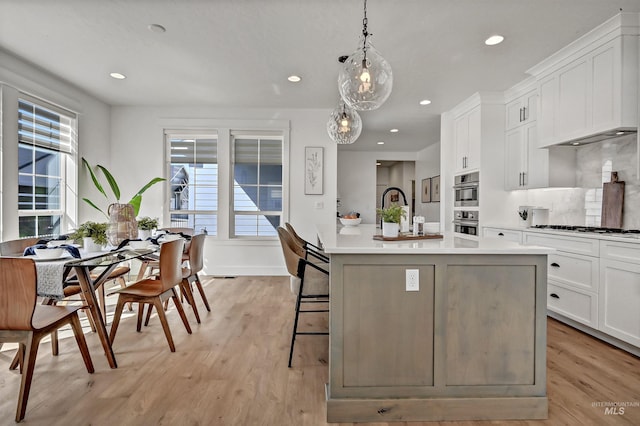 kitchen with gas cooktop, light wood-style flooring, light countertops, white cabinets, and decorative light fixtures