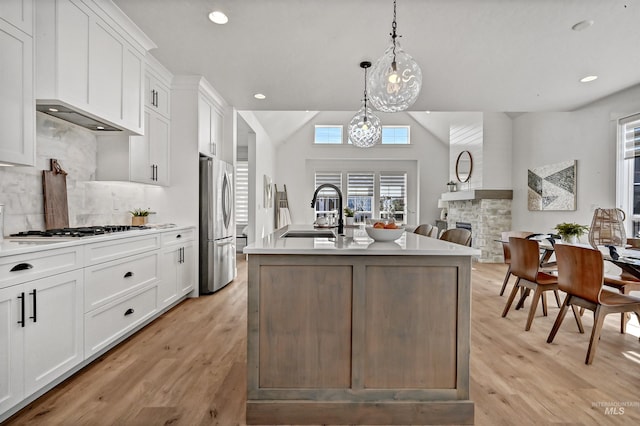 kitchen featuring light wood finished floors, a fireplace, stainless steel appliances, a sink, and white cabinetry