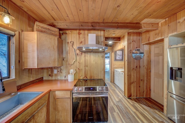 kitchen with appliances with stainless steel finishes, wall chimney exhaust hood, and wood walls