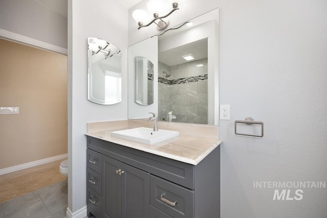 bathroom with a tile shower, tile patterned flooring, vanity, and toilet