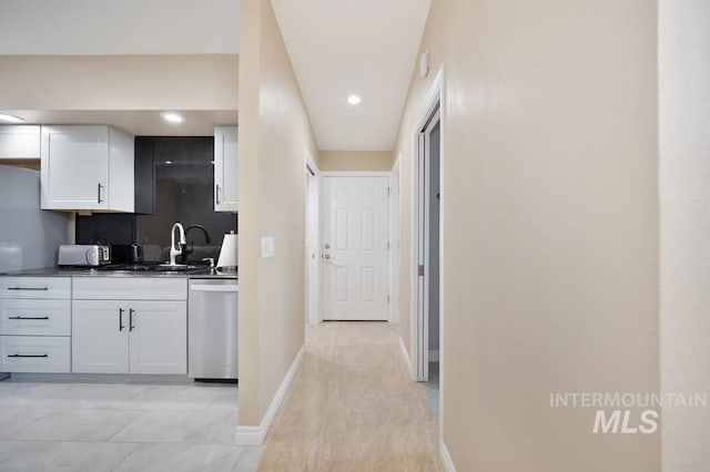 kitchen featuring white cabinets, sink, stainless steel dishwasher, decorative backsplash, and light tile patterned floors