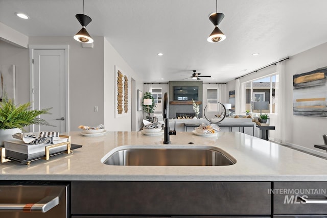 kitchen featuring open floor plan, a lit fireplace, hanging light fixtures, a ceiling fan, and a sink