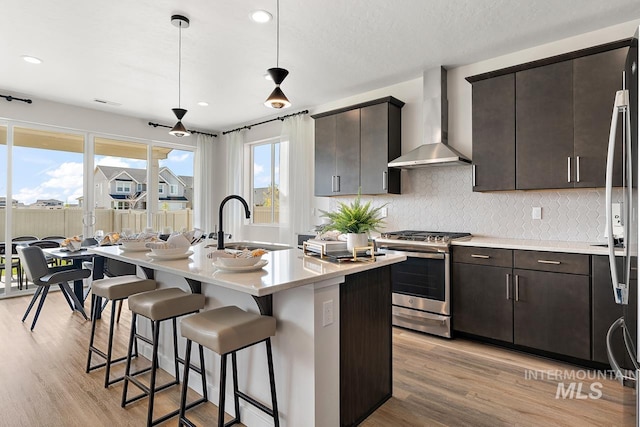 kitchen featuring wall chimney range hood, stainless steel range with gas stovetop, a breakfast bar area, decorative backsplash, and light wood-style flooring