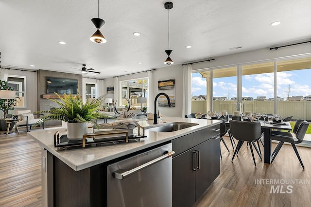 kitchen featuring decorative light fixtures, dishwasher, an island with sink, light wood-style flooring, and a sink