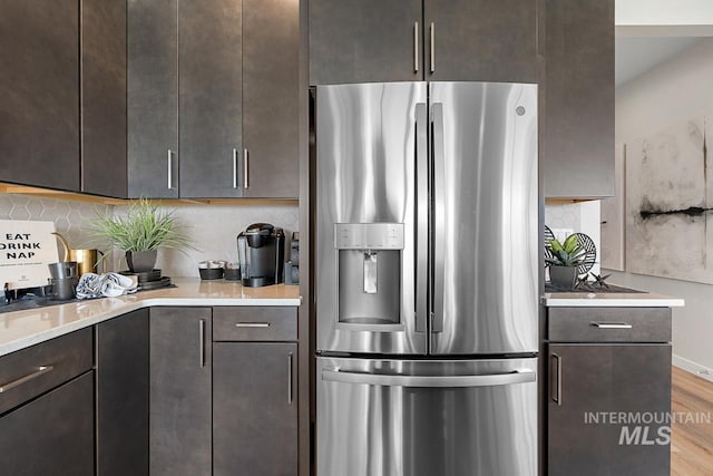 kitchen with decorative backsplash, dark brown cabinetry, light countertops, stainless steel refrigerator with ice dispenser, and light wood-type flooring