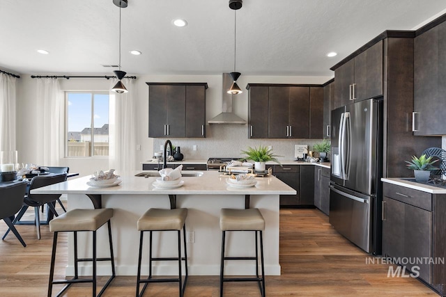 kitchen with a kitchen bar, a sink, appliances with stainless steel finishes, wall chimney exhaust hood, and light countertops