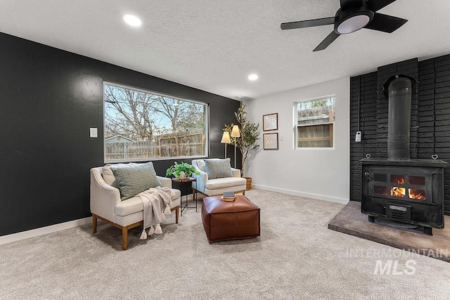 living area featuring ceiling fan, a wood stove, light carpet, and a textured ceiling