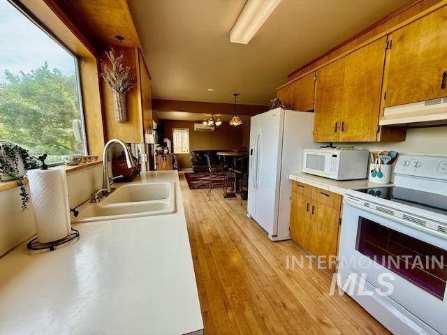 407 1st St, Asotin, WA 99402 - kitchen featuring white appliances, under cabinet range hood, brown cabinetry, light countertops, and hanging light fixtures