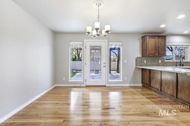 unfurnished dining area featuring recessed lighting, an inviting chandelier, a sink, baseboards, and light wood-style flooring