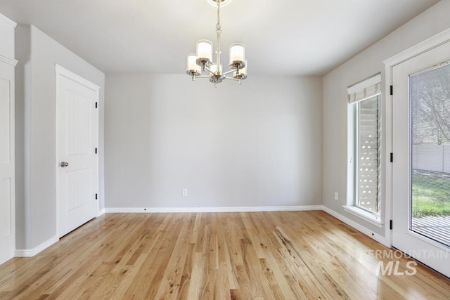 spare room featuring light wood-style flooring, baseboards, and an inviting chandelier