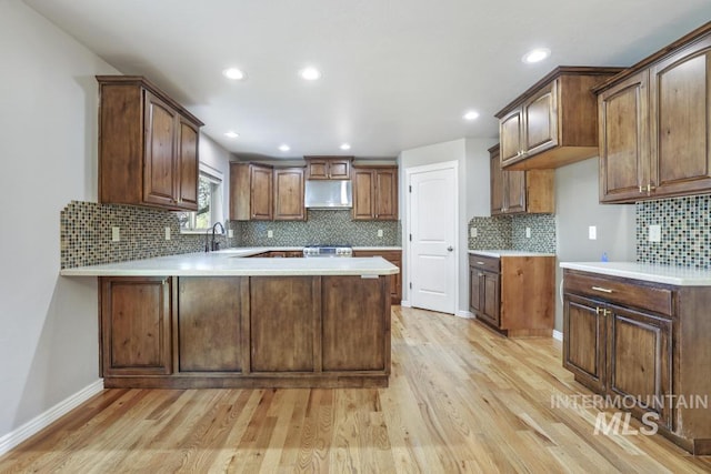 kitchen featuring extractor fan, light wood-style floors, light countertops, backsplash, and a peninsula