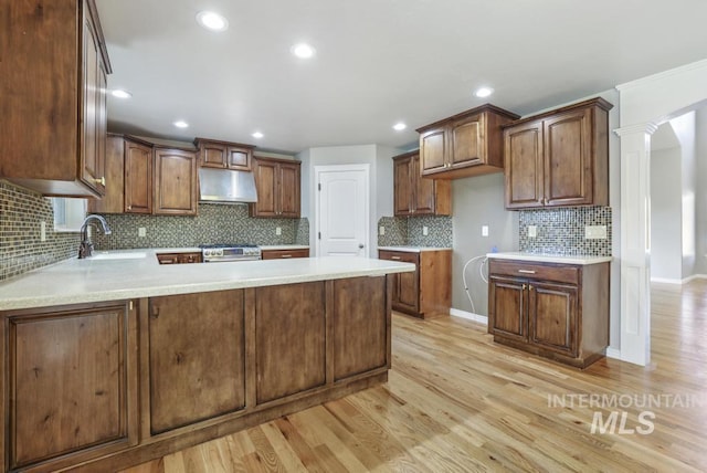 kitchen with a peninsula, a sink, light wood-type flooring, stainless steel gas stove, and under cabinet range hood