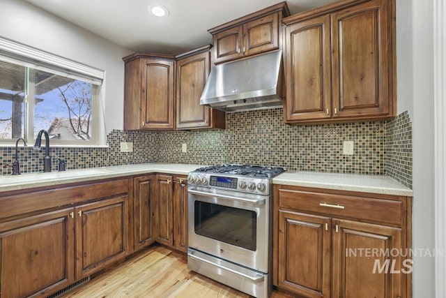 kitchen with gas stove, light countertops, under cabinet range hood, and a sink