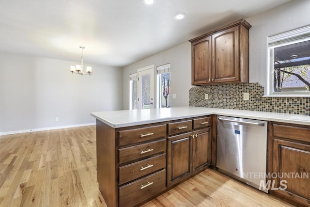 kitchen with stainless steel dishwasher, light wood-style flooring, an inviting chandelier, light countertops, and a peninsula