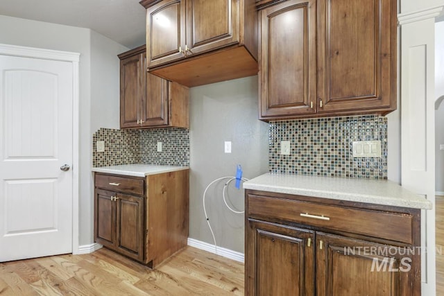 kitchen featuring light wood finished floors, decorative backsplash, light countertops, and baseboards
