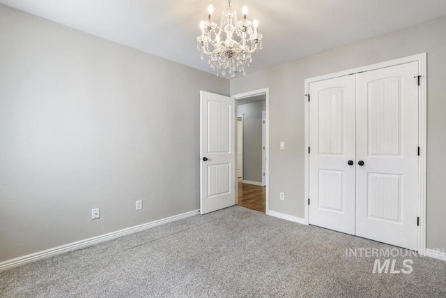unfurnished bedroom featuring an inviting chandelier, baseboards, carpet floors, and a closet