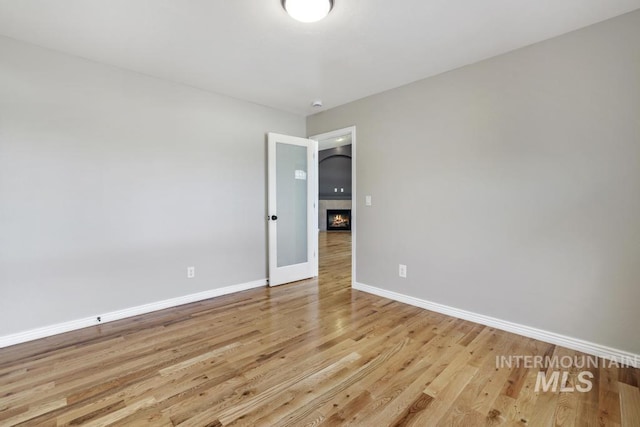 spare room with light wood finished floors, a tiled fireplace, and baseboards
