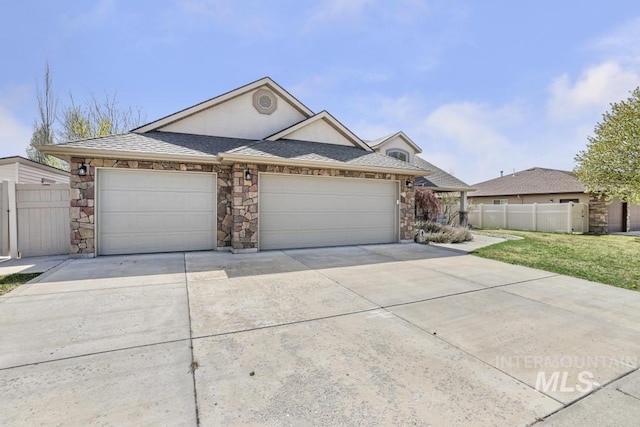 view of front of property with an attached garage, stone siding, fence, and driveway