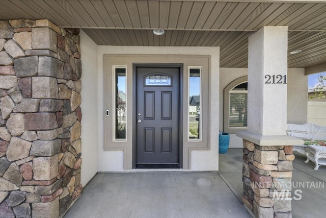 entrance to property featuring stucco siding, stone siding, and covered porch