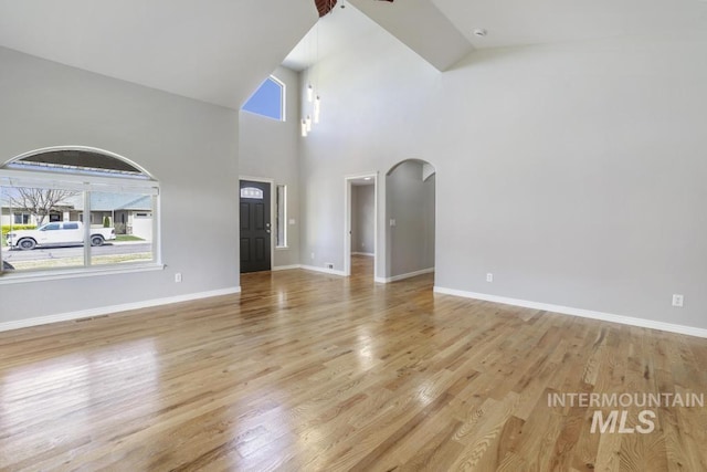 unfurnished living room with arched walkways, wood finished floors, and a wealth of natural light
