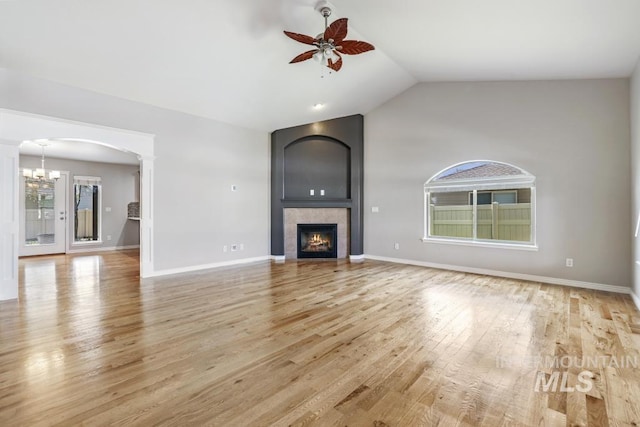 unfurnished living room with light wood finished floors, vaulted ceiling, decorative columns, a tiled fireplace, and ceiling fan with notable chandelier